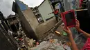 Seorang warga saat mengambil gambar rumah yang rubuh dikawasan muara baru, Jakarta, Jumat (13/2/2015).  Sebanyak 33 rumah di muara baru Jakarta Utara mengalami kemiringan parah dan 2 buah rumah ambruk akibat banjir. (Liputan6.com/Faizal Fanani)