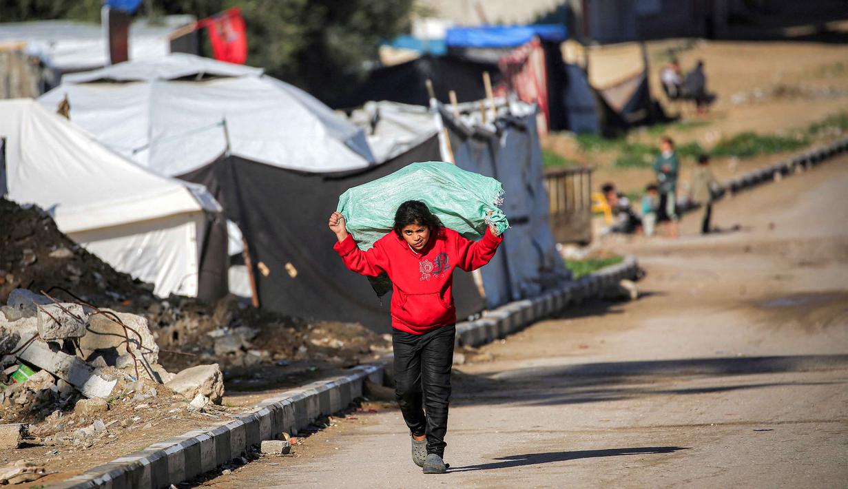 Penelitian tersebut juga menyoroti bahwa anak-anak di Gaza saat ini berada dalam kondisi terlalu lapar, trauma, dan kelelahan untuk dapat belajar atau bermain, yang mengancam masa depan mereka secara permanen. Tampak dalam foto, seorang gadis kecil membawa karung di punggungnya sambil berjalan di sepanjang jalan di kamp pengungsi Nuseirat untuk pengungsi Palestina di utara Deir al-Balah, Jalur Gaza tengah pada 29 Januari 2026. (EYAD BABA/AFP)
