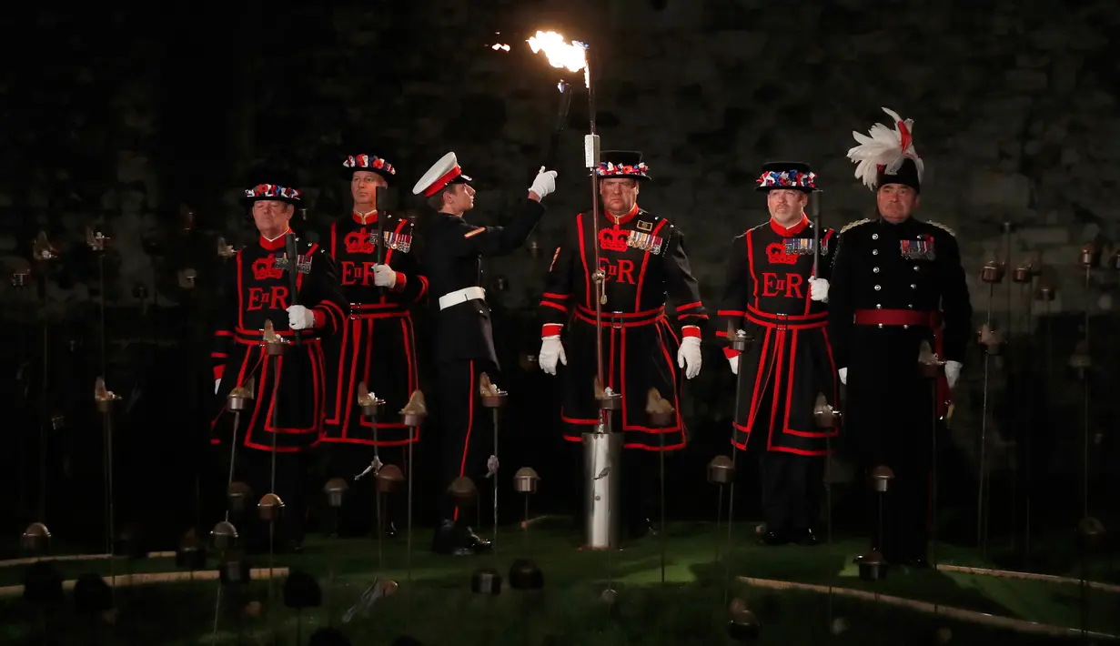 Yeoman Warders atau 'Beefeaters' menyaksikan British Royal Marine menyalakan api untuk menghidupkan ribuan lilin di parit kering Tower of London, Inggris, Selasa (6/11). Lilin itu untuk menandai 100 tahun akhir Perang Dunia I. (AP Photo/Alastair Grant)
