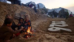 Dan, lebih dari 171.222 orang mengalami luka-luka, banyak di antaranya menderita cedera permanen yang mengubah hidup. Tampak dalam foto, anak-anak menghangatkan diri di dekat api unggun di samping patung pasir karya seniman Yazed Abo Jarad yang menggambarkan tahun mendatang di Deir El-Balah, Jalur Gaza tengah pada 30 Desember 2025. (Bashar Taleb/AFP)