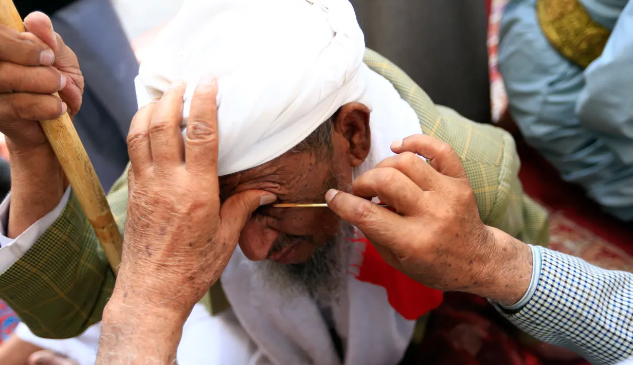 Seorang pria Yaman mengoleskan kosmetik tradisional kohl ke kelopak mata pria lain di Masjid Agung, kota tua Sanaa pada 9 mei 2019. Bagi muslim Yaman, pemakaian kohl diyakini mampu membersihkan dan melindungi mata dari penyakit ini sudah menjadi tradisi setiap bulan Ramadan. (MOHAMMED HUWAIS/AFP)