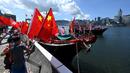 Orang-orang mengibarkan bendera sebagai kapal penangkap ikan dengan spanduk dan bendera untuk menandai peringatan 25 tahun Penyerahan Hong Kong dari Inggris ke China berlayar melalui pelabuhan Victoria Hong Kong (28/6/2022). (AFP/Peter Parks)