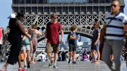 Turis berjalan di depan Menara Eiffel, Paris, Kamis (2/8). Dua hari terakhir atau sejak Rabu (1/8), karyawan menara yang menjulang setinggi 324 meter ini mogok. (AFP PHOTO/GERARD JULIEN)