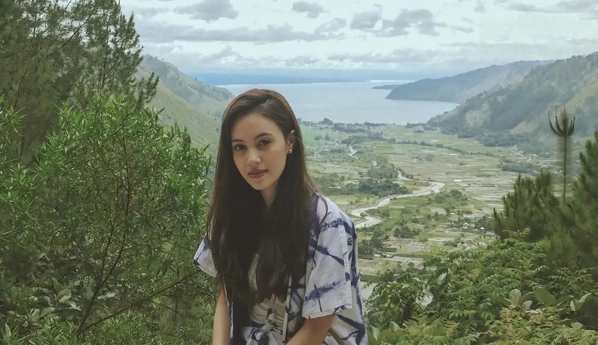 Pemeran Mia di film Yowis Ben 2 ini terlihat sangat cantik berpose dengan latar belakang Danau Toba. Menggunakan pakaian putih bercorak biru, rambutnya yang panjang tampak memesona. (Liputan6.com/IG/@anggikabolsterli)