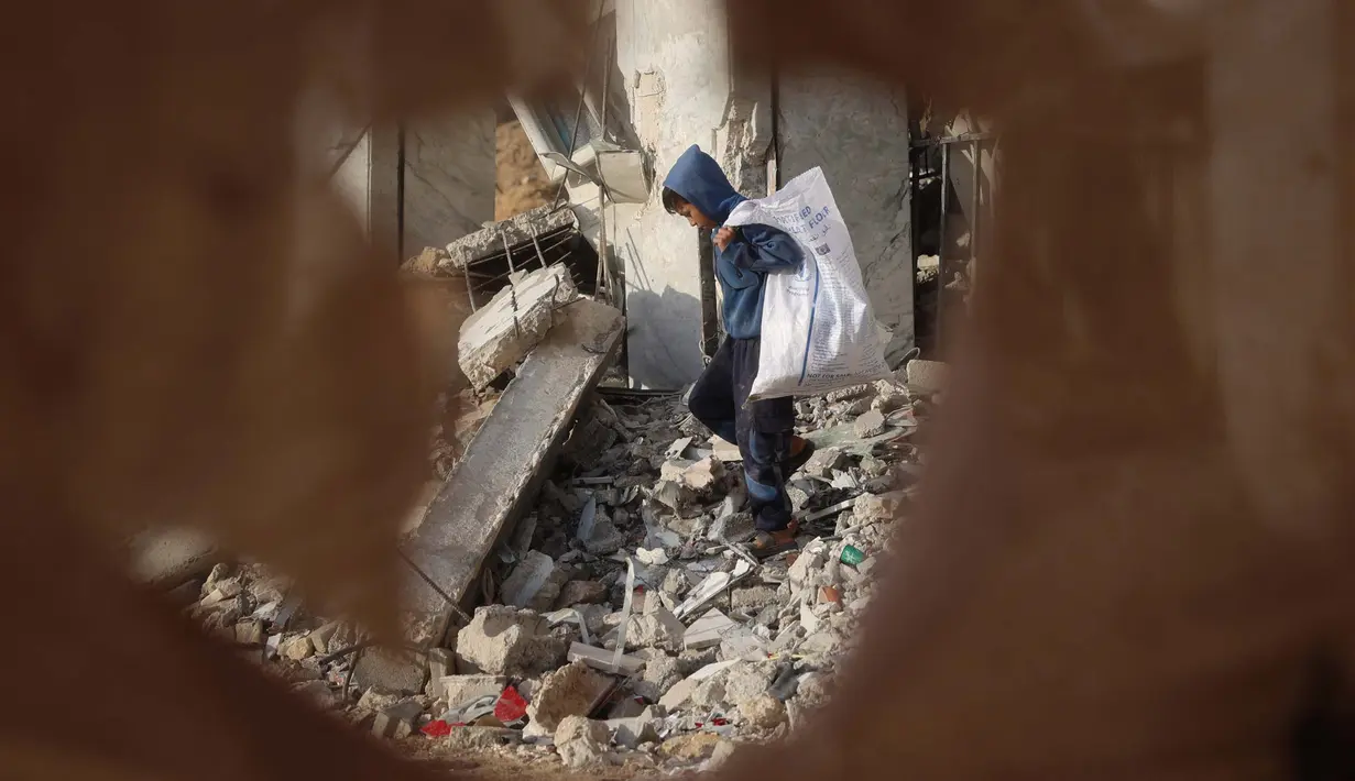 Perayaan Hari Anak Sedunia 2024 tidak bisa dirasakan oleh anak-anak yang berada di wilayah konflik. Tampak dalam foto, seorang anak laki-laki Palestina mengumpulkan barang-barang yang bisa diselamatkan dari puing-puing bangunan yang hancur akibat seragan Israel di Khan Yunis, Jalur Gaza selatan pada 19 November 2024. (Eyad BABA/AFP)