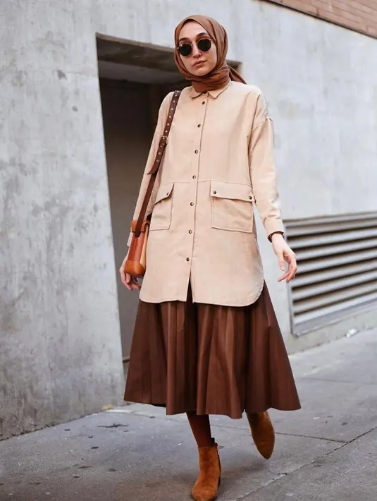 Buat kesan hangat pada tampilanmu dengan memadukan tunik warna cream bersama rok plisket dan hijab warna cokelat yang senada. Pilihan sepatu suede boots bikin look-mu makin kece. (Instagram/elifd0gan).