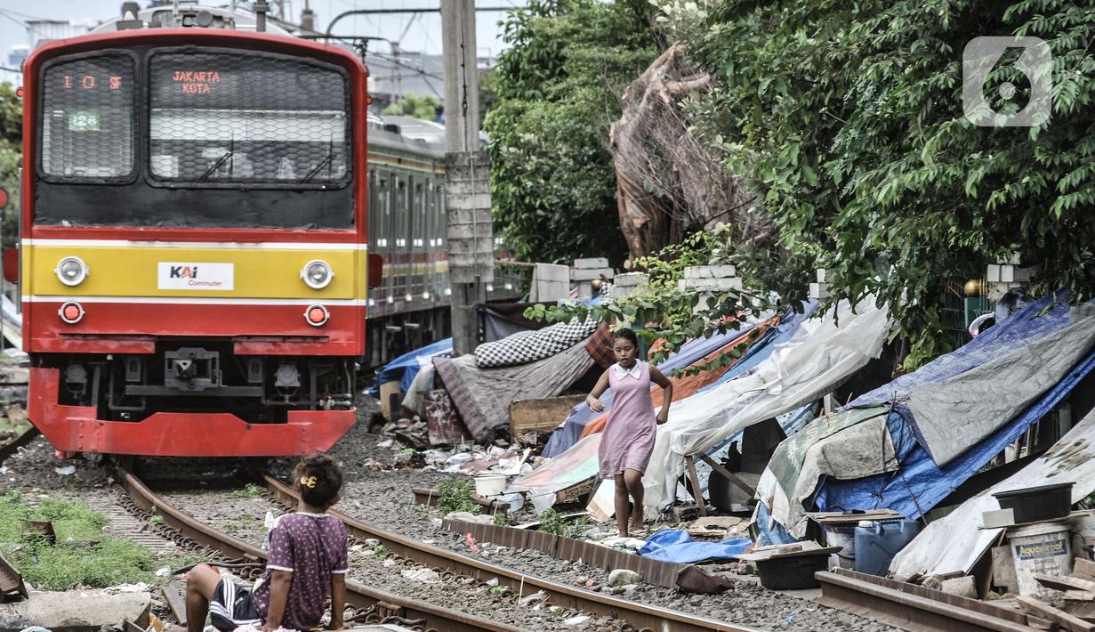 Kereta commuterline melintas di dekat deretan bangunan semipermanen milik tunawisma di kawasan Senen, Jakarta, Minggu (14/2/2021). Sebelumnya pada 2014, pihak KAI membongkar ratusan gubuk tunawisma demi keselamatan perjalanan kereta api serta warga di bantaran rel. (merdeka.com/Iqbal S. Nugroho)
