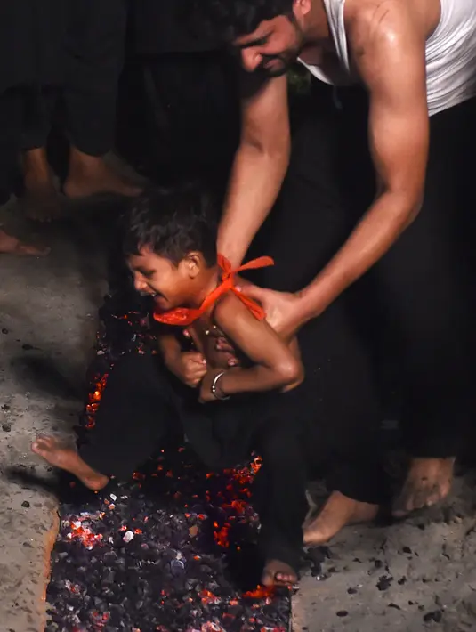 Seorang umat Syiah Pakistan membawa anak kecil untuk berlari di atas bara api saat peringatan Hari Asyura di Lahore, Rabu (19/9). Umat Syiah Pakistan akan memperingati Hari Asyura pada 21 September 2018. (ARIF ALI/AFP)