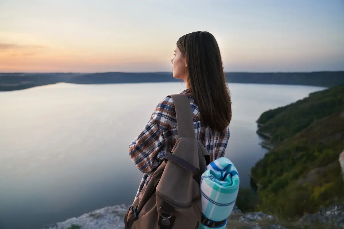 Seorang perempuan sedang menikmati sunset di tepi tebing (Foto Dok: Freepik/serhii_bobyk)