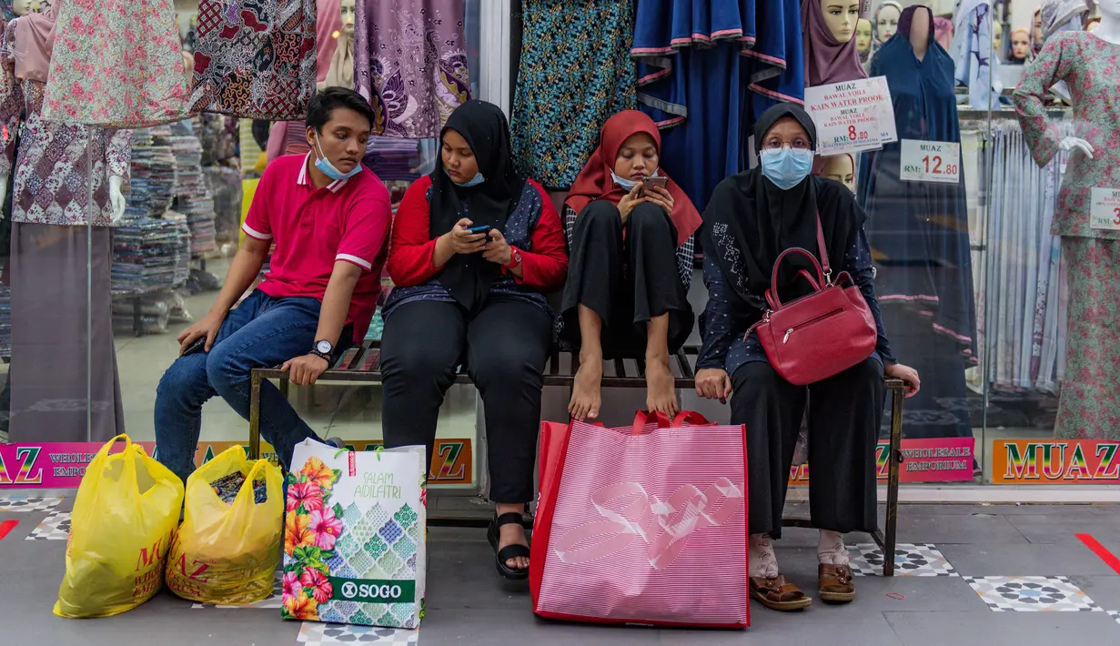 Keluarga yang mengenakan masker untuk mengantisipasi penyebaran virus corona COVID-19 duduk di luar toko setelah berbelanja menjelang Idul Fitri di Kuala Lumpur, Malaysia, Kamis (21/5/2020). Hari Raya Idul Fitri menandai berakhirnya bulan suci Ramadan. (Mohd RASFAN/AFP)