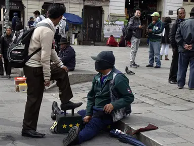 Tukang semir sepatu bertopeng melayani pelanggannya di kawasan La Paz, Bolivia (29/11). Dengan menutup wajahnya para tukang semir ini menyembunyikan identitas karena pekerjaan tersebut dipandang rendah oleh masyarakat lokal. (AFP PHOTO/Aizar Raldes)