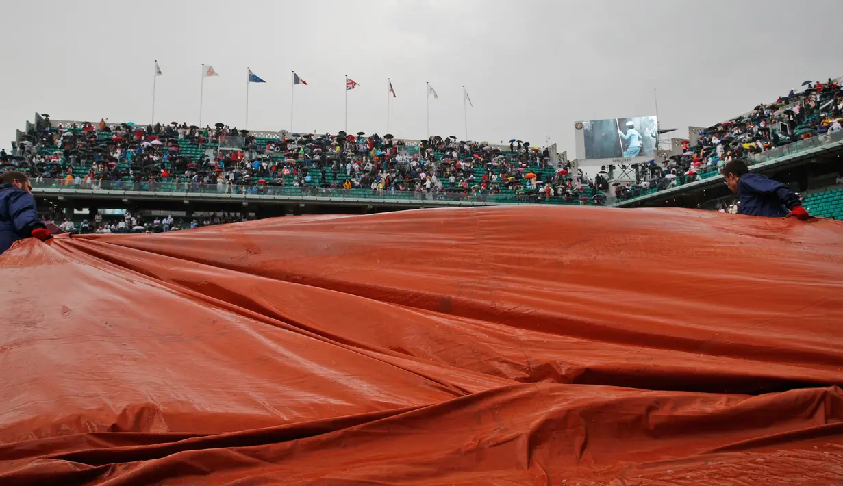 Pekerja stadion menarik penutup lapangan usai pertandingan perempat final Perancis Terbuka ditunda di stadion Roland Garros, Paris (6/6). Pertandingan antara Rafael Nadal dan Diego Schwartzman sempat ditunda karena hujan. (AP/Christophe Ena)