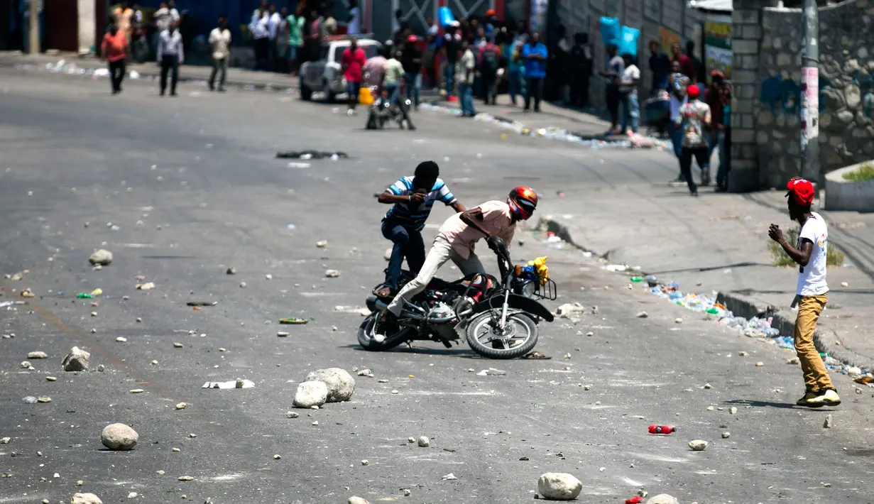 Dua pria jatuh dari sepeda motor setelah pengunjuk rasa melemparinya dengan batu karena berusaha melewati barikade yang dibuat dalam protes krisis bahan bakar di Port-au-Prince, Haiti, Senin (16/9/2019). Protes menyebabkan bank dan kantor pemerintahan tutup. (AP Photo/Dieu Nalio Chery)