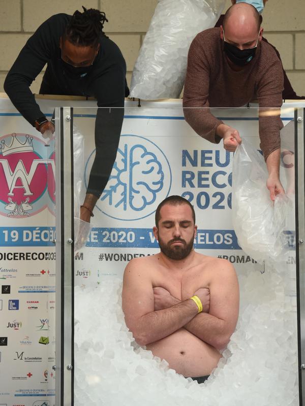 Seorang pria memasukkan es batu saat Romain Vandendorpe mencoba memecahkan rekor dunia di Wattrelos, Prancis, 19 Desember 2020. Vandendorpe di dalam es di kabin kaca transparan selama 2 jam, 35 menit dan 43 detik, memecahkan rekor sebelumnya yakni 40 menit di kota Wattrelos. (FRANCOIS LO PRESTI/AFP)