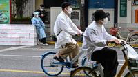 Seorang pekerja yang mengenakan alat pelindung diri berdiri dekat kotak untuk dikirim sementara dua orang mengendarai sepeda saat perberlakuan lockdown karena virus corona COVID-19 di Distrik Jing'an, Shanghai, China, Rabu (18/5/2022). (Hector RETAMAL/AFP)