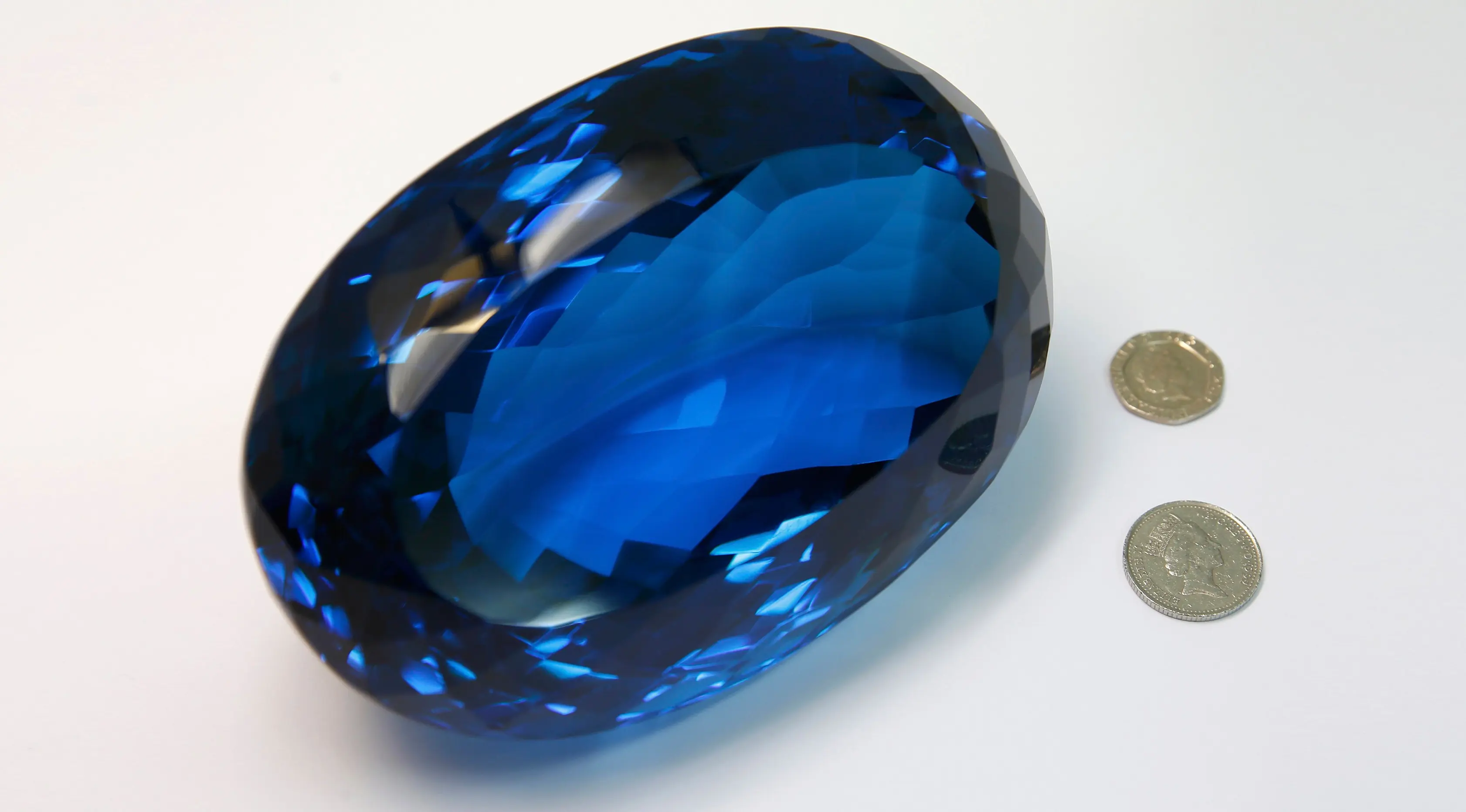 Batu permata jenis topaz berwarna biru disandingkan dengan uang koin di Museum Sejarah Alam London, Inggris, Selasa (27/9). Batu milik Maurice Ostro ini menjadi batu topaz terbesar di dunia. (REUTERS / Peter Nicholls)