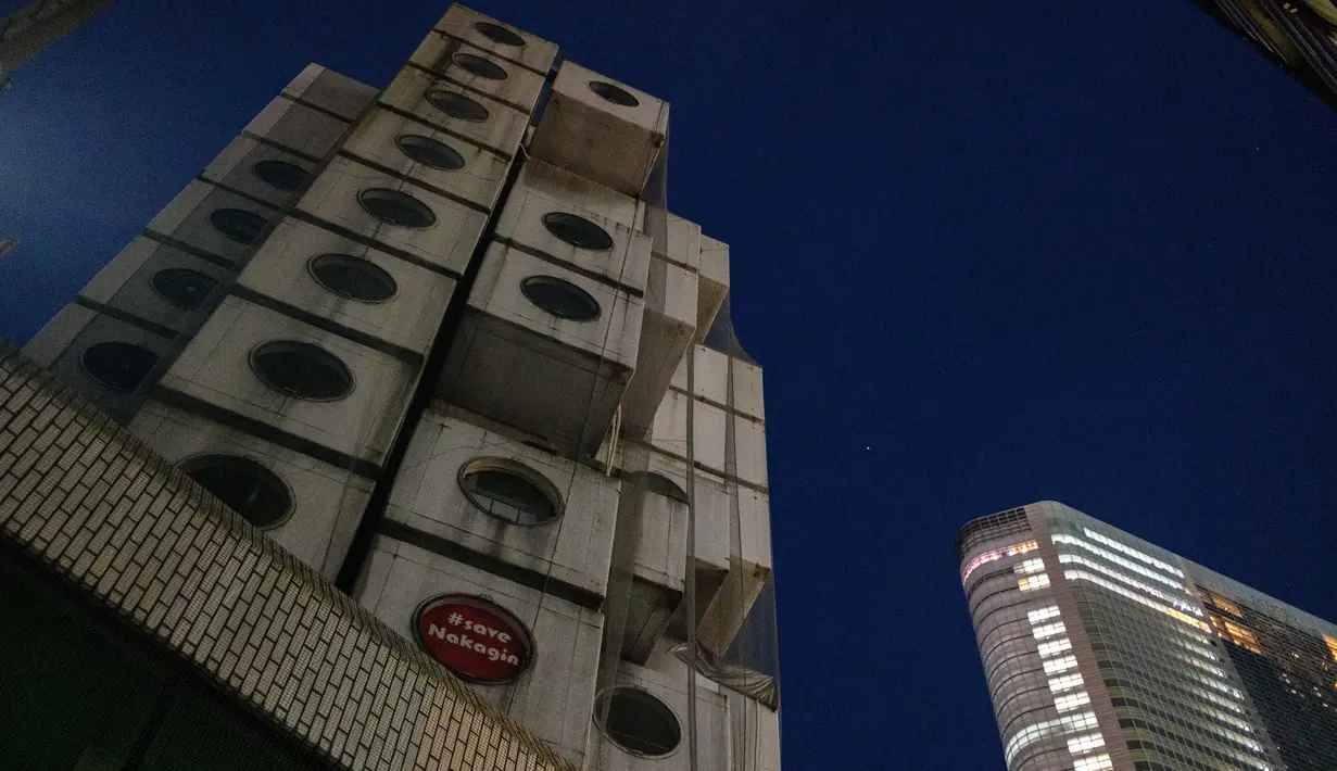 Menara Kapsul Nakagin yang terkenal (kiri) terlihat di distrik Ginza Tokyo, 6 April 2022. Seiring berjalannya waktu, kondisi bangunan tersebut memburuk. Wacana mengenai penghancurannya telah dimulai dari 2006, namun ide tersebut tidak diwujudkan hingga tahun ini. (Philip FONG/AFP)