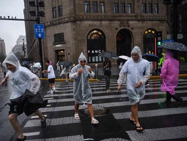 Orang-orang melindungi diri mereka dengan mantel hujan sekali pakai selama perjalanan Topan Co-May di Shanghai pada tanggal 30 Juli 2025. (Hector RETAMAL/AFP)