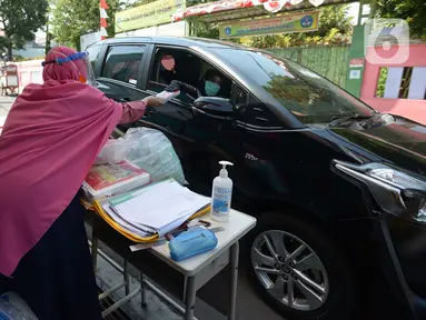 Guru SDIT Ibnu Sina memberikan tugas sekolah secara drive-thru kepada wali murid di Jakarta, Rabu (26/8/2020). Selama pembelajaran jarak jauh, siswa diwajibkan mengambil dan mengembalikan tugas di sekolah. (merdeka.com/Imam Buhori)