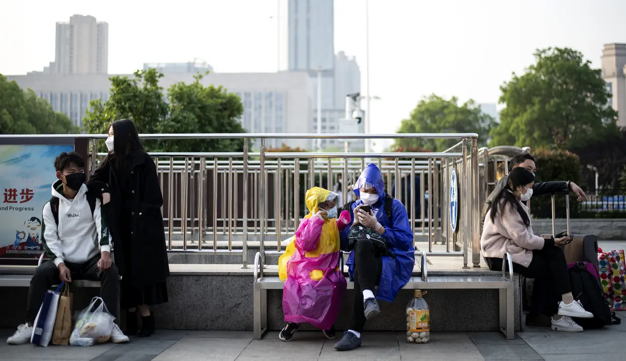 Warga yang mengenakan masker dan pakaian pelindung duduk di luar Stasiun Hankou, Wuhan, Hubei, China, Rabu (8/4/2020). Setelah pandemi virus corona COVID-19 mereda, banyak warga di Wuhan beraktivitas memakai masker, sarung tangan, pelindung wajah, hingga pakaian pelindung. (NOEL CELIS/AFP)