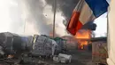 Sebuah bendera Prancis berada di dekat Kobaran api yang membakar sebuah kamp pengungsian imigran selama pembongkaran kamp pengungsian imigran "Jungle", di kota pelabuhan Calais, Prancis (26/10). (REUTERS/Pascal Rossignol)
