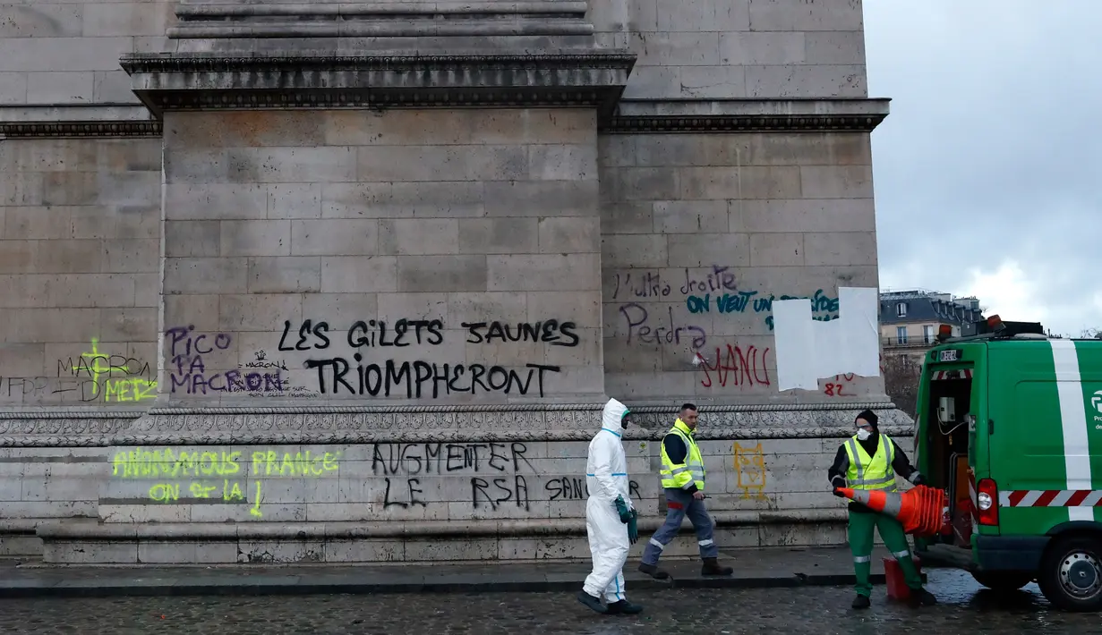 Pekerja membersihkan grafiti bertuliskan 'jaket kuning akan menang' di Arc de Triomphe, Paris, Prancis, Minggu (2/12). Kenaikan pajak bahan bakar memicu kerusuhan di Paris. (AP Photo/Thibault Camus)