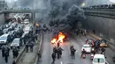 Polisi anti huru-hara tiba ketika pengemudi taksi memblokir jalan dengan membakar ban saat unjuk rasa menentang layanan transportasi VTC seperti Uber, di jalan lingkar di porte Maillot di Paris, Perancis, Selasa (26/1). (AFP PHOTO/Thomas SAMSON)
