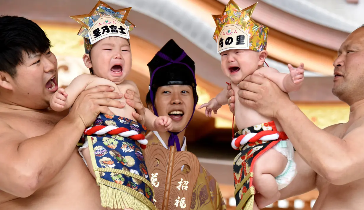 Dua pesumo menggendong bayi yang menangis selama Festival Nakizumo atau kontes bayi menangis di kuil Kamegaike-Hachiman, Jepang, Minggu (14/5). Lebih dari 100 bayi mengikuti kontes menangis yang diyakini bisa membuat bayi sehat. (Toru YAMANAKA/AFP)