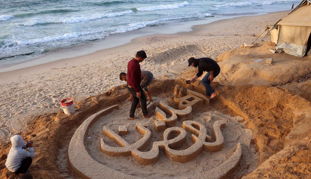 Warga membantu seniman Palestina, Yazeed Abu Jarad, saat ia membuat patung pasir dengan pesan ucapan "Selamat Datang, Ramadan" di sepanjang pantai di Khan Younis, selatan Gaza pada 17 Februari 2026. (Bashar Taleb/AFP)