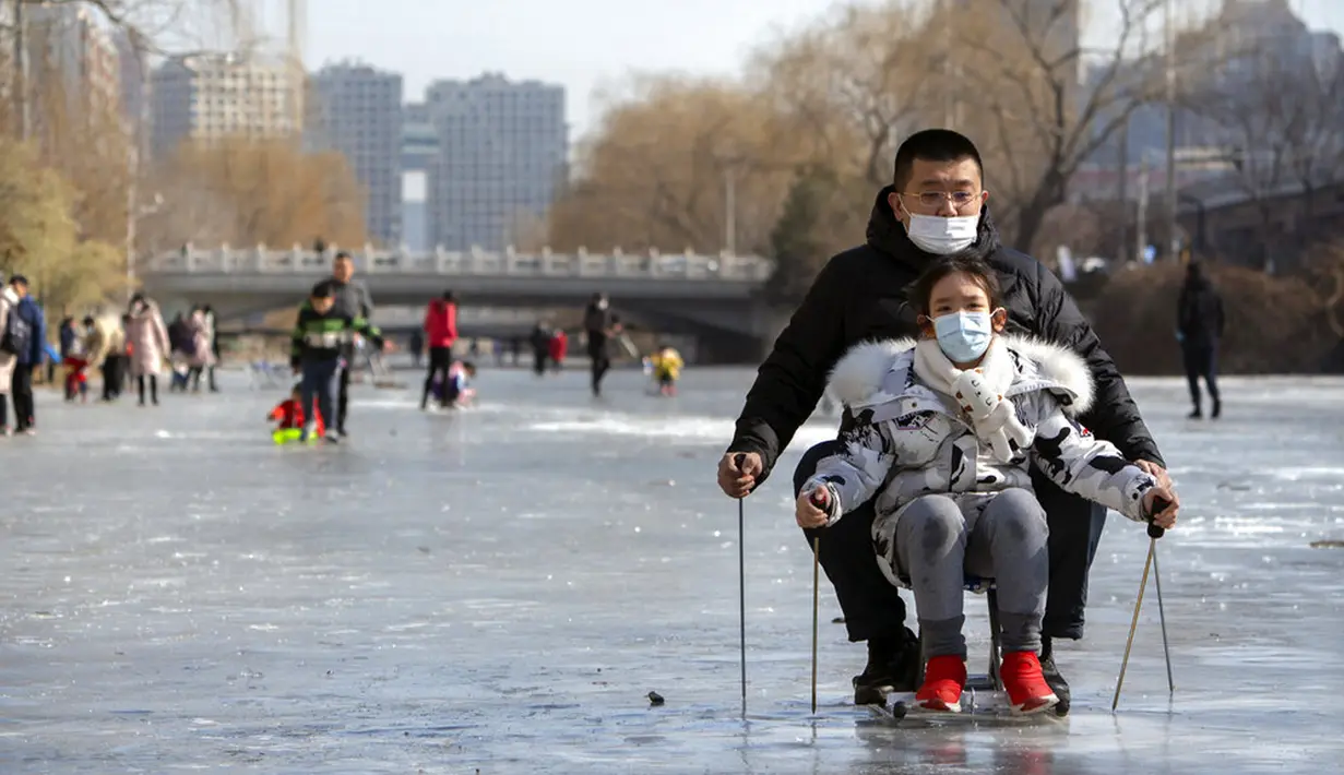 Orang-orang yang memakai masker wajah untuk melindungi dari penyebaran virus corona COVID-19 menggunakan kursi untuk meluncur melintasi permukaan kanal yang membeku di Beijing, China, Sabtu (30/1/2021). (AP Photo/Mark Schiefelbein)