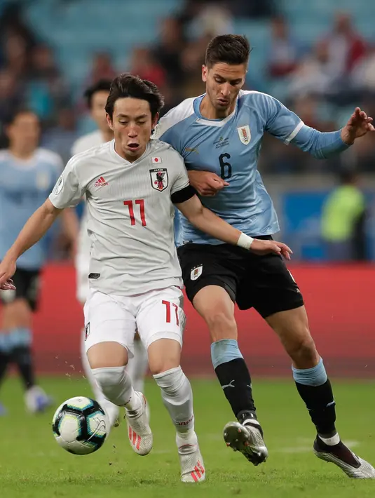 Gelandang Jepang, Koji Miyoshi menggiring bola dari kawalan gelandang Uruguay, Rodrigo Bentancur  selama pertandingan grup C Copa America 2019 di Arena Gremio di Porto Alegre, Brasil (20/6/2019). Koji Miyoshi mencetak dua gol dipertandingan ini.  (AP Photo/Silvia Izquierdo)