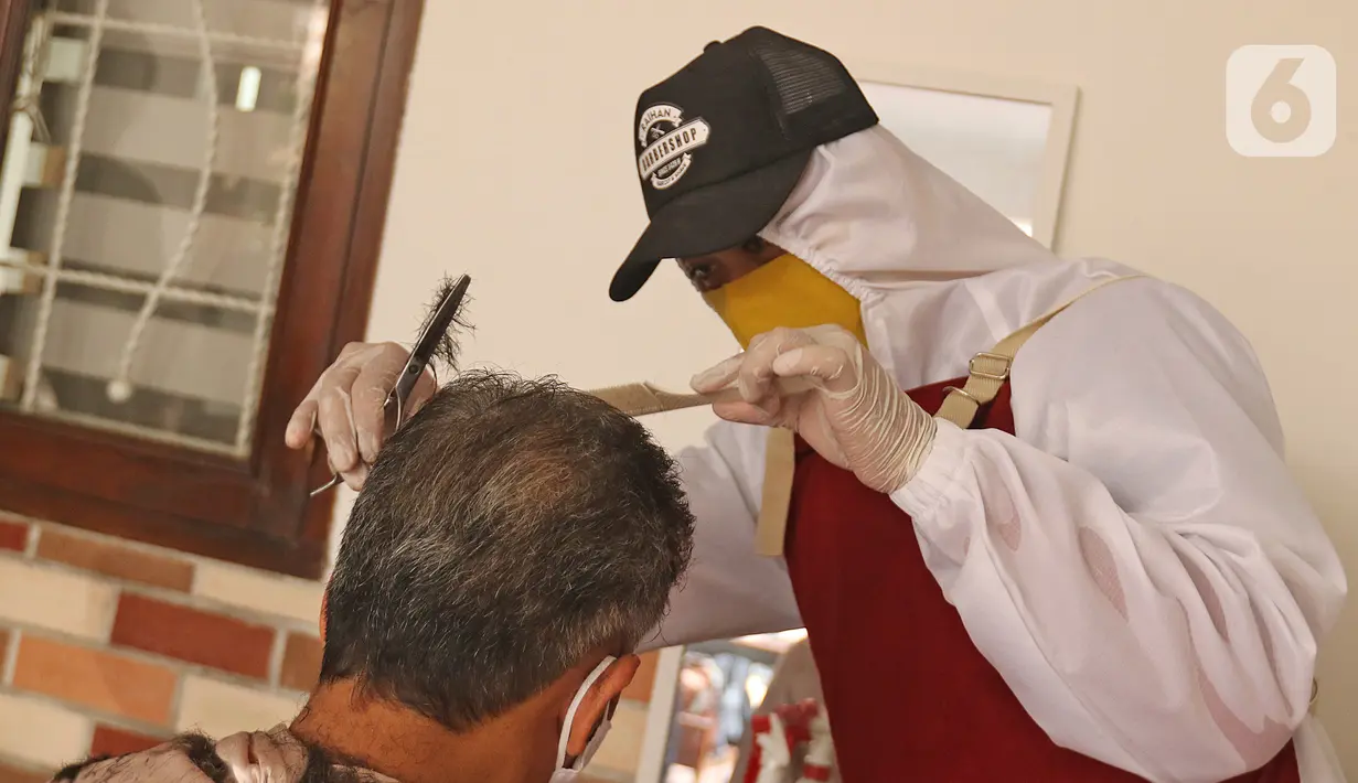 Tukang cukur mengenakan APD saat memotong rambut di halaman rumah pelanggan, Kelapa Dua, Depok, Jawa Barat, Senin (27/4/2020). Penerapan PSBB Kota Depok membuat tukang cukur tersebut menerima jasa panggilan ke rumah dan mengenakan APD untuk mencegah penularan COVID-19. (Liputan6.com/Herman Zakharia)