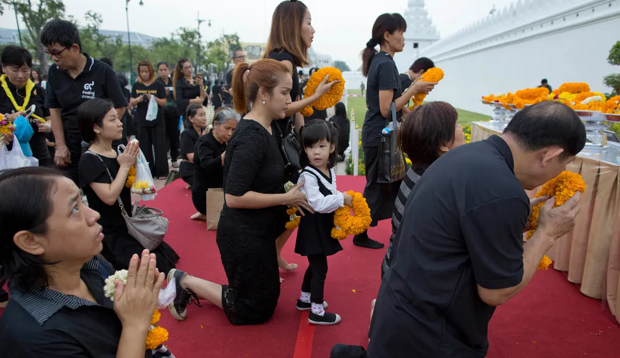 Warga Thailand mengenakan pakain hitam dan membawa bunga saat memberi penghormatan untuk mendiang Raja Thailand Bhumibol Adulyadej di luar Grand Palace, Bangkok, Thailand (13/10). (AP Photo/Gemunu Amarasinghe)
