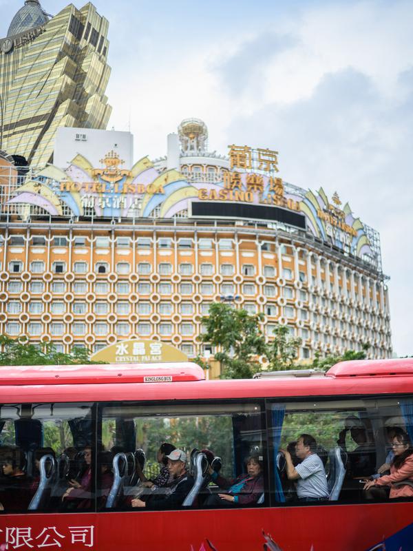 Wisatawan duduk dalam bus dengan latar belakang resor kasino Grand Lisboa (kiri) di Macau, 5 Maret 2019. Macau saat ini memiliki lebih dari 30.000 kamar tamu yang tersebar di 75 properti hotel bintang dua hingga lima. (Anthony Wallace/AFP)