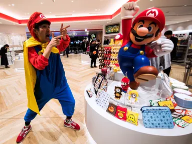 Seorang pria mengenakan kostum salah satu tokoh ikonik dari Nintendo, Mario berpose di sebelah merchandise yang berkaitan dengan permainan ini selama pratinjau pers di toko baru Nintendo di Tokyo, 19 November 2019. Nintendo akan meresmikan toko pertamanya di Tokyo pada pekan ini. (Behrouz MEHRI/AFP)