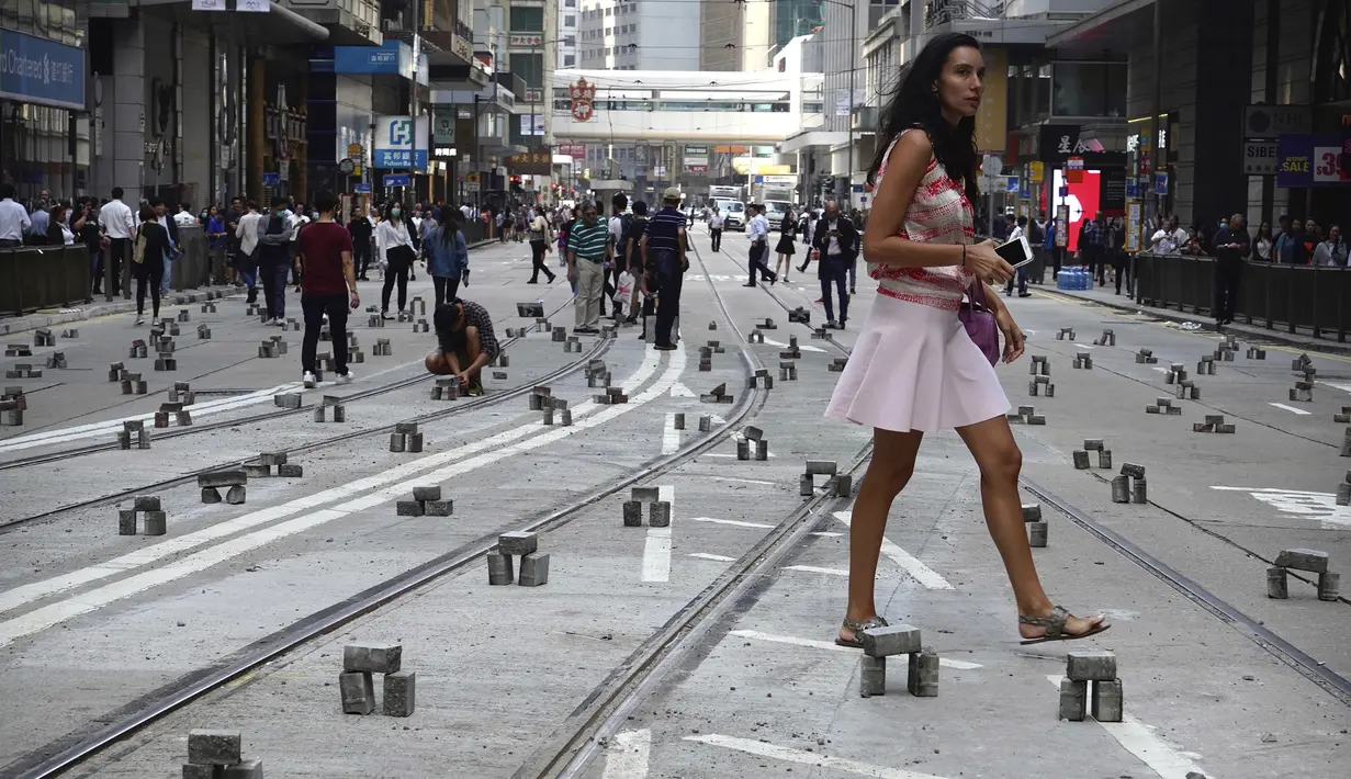Seorang wanita berjalan melewati batu bata yang ditempatkan  demonstran untuk menghalangi jalan selama protes di distrik keuangan di Hong Kong (14/11/2019). (AP Photo/Vincent Yu)