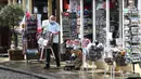 Seorang pemilik toko suvenir mengeluarkan barang dagangannya saat bisnis kembali buka di Windsor, barat London, Senin (12/4/2021). Inggris melonggarkan pembatasan terkait virus corona COVID-19. (Photo by Paul ELLIS/AFP)