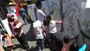 Pejalan kaki melintas dekat sejumlah anak yang melukis mural pada dinding areal gang sempit di Pulo Gelis, Bogor, Minggu (18/3). Kegiatan ini untuk menjadikan Kampung Pulo Geulis sebagai salah satu tujuan wisata baru di Bogor. (Merdeka.com/Arie Basuki)