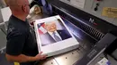 Pekerja di kantor penerbitan pemerintah AS, Daniel Kinney memotong tepi foto Presiden Amerika Serikat Donald Trump di Washington DC (4/12). (Chip Somodevilla/Getty Images/AFP)