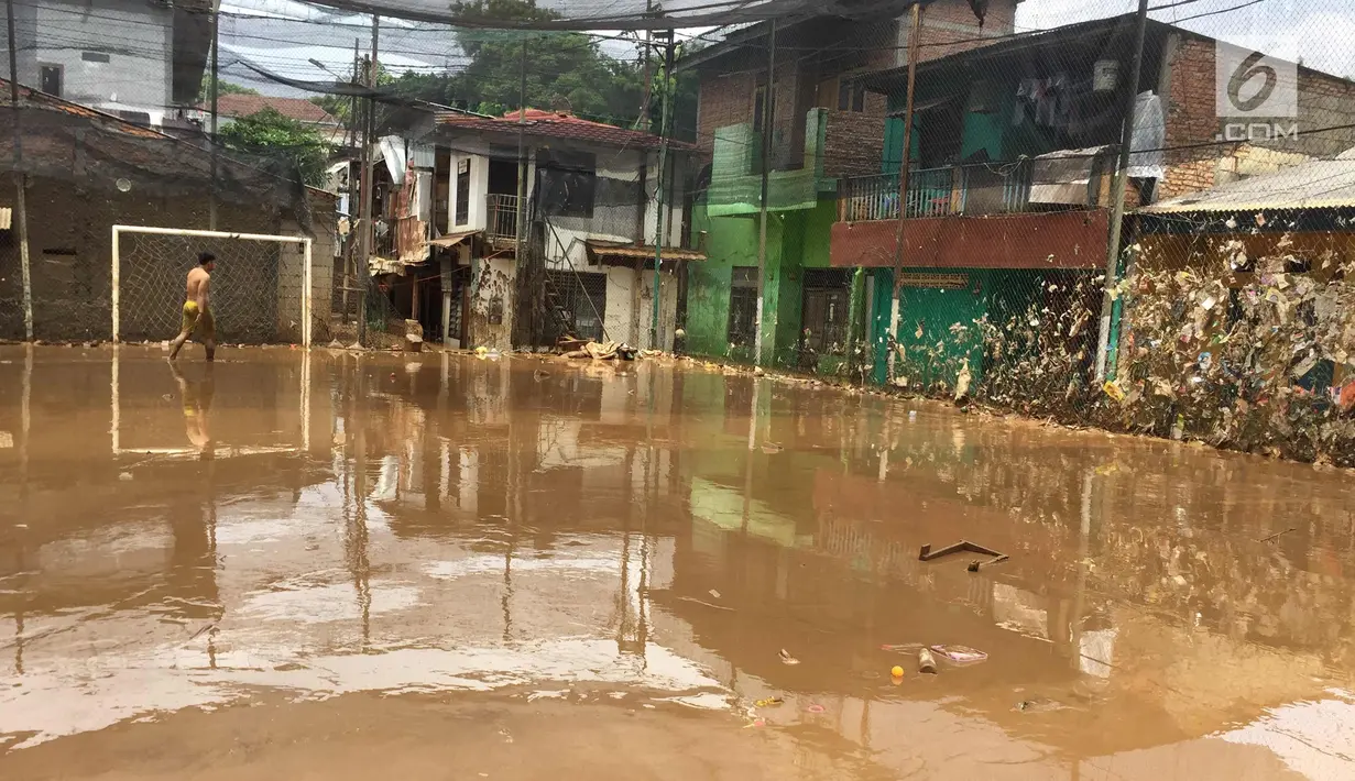 Warga melintas di lapangan futsal yang diselimuti sampah dan lumpur di kawasan Rawajati, Jakarta, Selasa (6/2). Banjir yang merendam kawasan tersebut menyebabkan lumpur dan sampah mengendap di setiap sudut. (Liputan6.com/Immanuel Antonius)