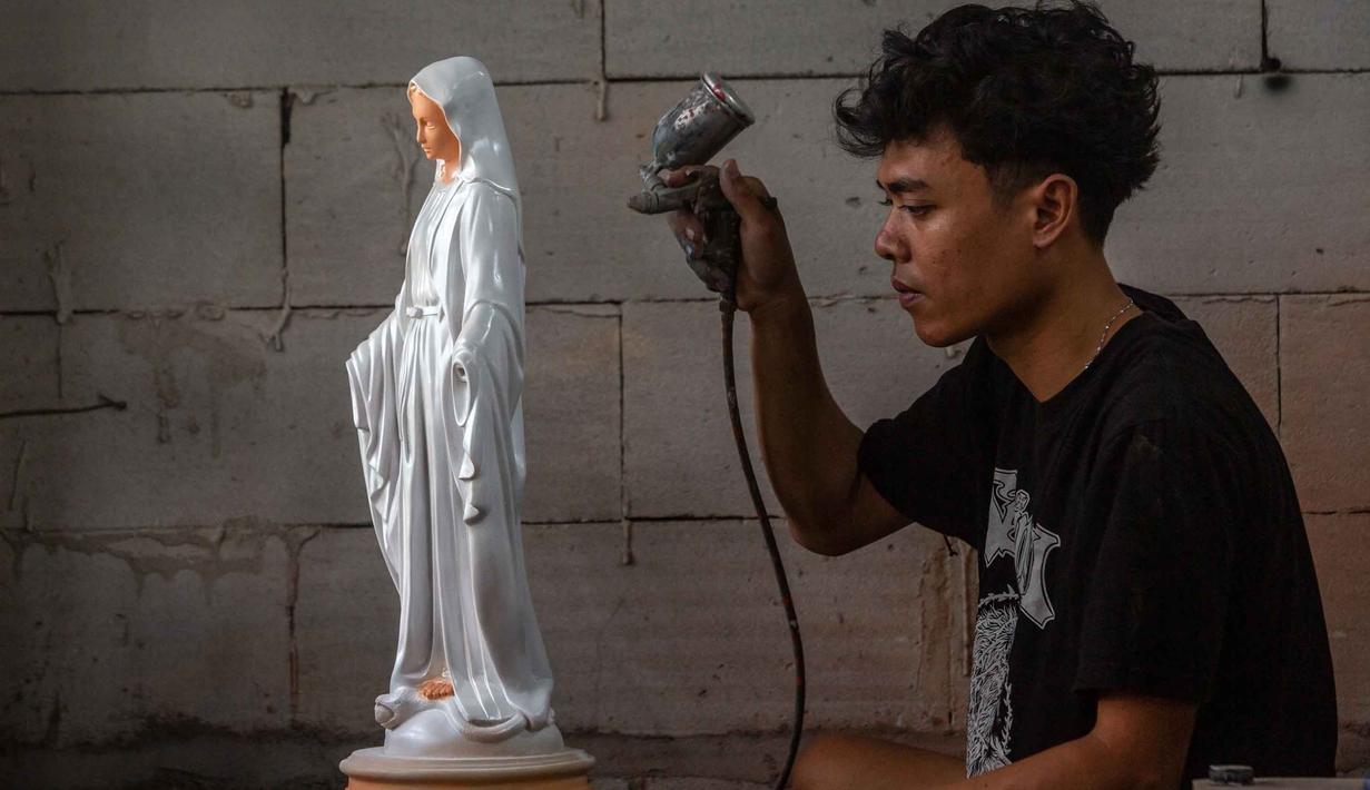 Biasanya, jelang perayaan Natal, bengkel ini mengalami peningkatan pesanan pembuatan patung rohani keagamaan Kristen dari berbagai daerah. Tampak dalam foto, seorang pekerja menyemprotkan cat pada patung keagamaan Kristen di bengkel kerajinan Studio Malta Jaya di Bantul, Yogyakarta, pada Kamis 18 Desember 2025. (DEVI RAHMAN/AFP)