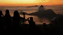 Turis berfoto saat matahari terbit dengan latar belakang gunung Sugarloaf dan teluk Guanabara di Bukit Corcovado di Rio de Janeiro, Brasil, pada 24 Maret 2023. (Photo by Carl DE SOUZA / AFP)