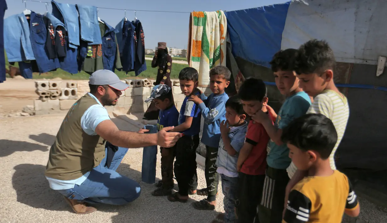<p>Seorang sukarelawan membagikan pakaian kepada anak-anak Suriah di sebuah kamp di pinggiran kota Dana yang dikuasai pemberontak, di sebelah timur perbatasan Turki-Suriah di provinsi barat laut Idlib (30/4/2022). Umat Islam seluruh dunia bersiap untuk merayakan Idul Fitri yang menandai akhir bulan puasa Ramadhan. (AFP/Aaref Watad)</p>