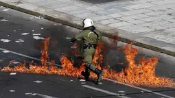 Polisi anti huru-hara melwati jalanan yang terbakar api di Athena, Yunani, (12/11/2015). Para Demonstran juga melakukan aksi mogok kerja selama 24 jam. (REUTERS/Yannis Behrakis)