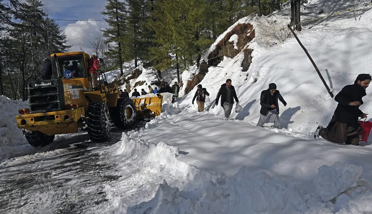 Para pekerja menggunakan alat berat untuk membersihkan jalanan usai badai salju menjebak kendaraan wisatawan di sepanjang jalan Bukit Murree, Pakistan, 9 Januari 2022. Sebanyak 22 wisatawan tewas saat sekitar 1.000 kendaraan terjebak salju tebal di Bukit Murree. (Aamir QURESHI/AFP)