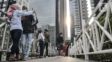 Warga berfoto di jembatan penyeberangan orang (JPO) tanpa atap di kawasan Sudirman, Jakarta, Minggu (4/4/2021). JPO tanpa atap masih menjadi wisata alternatif warga ibu kota dalam menghabiskan waktu akhir pekan untuk berfoto-foto dengan latar belakang gedung perkantoran (merdeka.com/Iqbal S Nugorho