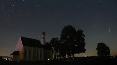 Sebuah meteor melintas di tengah langit malam selama hujan meteor tahunan Perseid di belakang gereja ziarah Sankt Coloman, barat daya Jerman, Minggu (12/8). Puncak hujan meteor terjadi pada 11-12 Agustus dan 12-13 Agustus. (KARL-JOSEF HILDENBRAND/DPA/AFP)