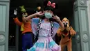 Seorang pengunjung yang mengenakan masker berswafoto dengan karakter kartun Goofy dan Pluto di Disneyland Hong Kong pada Jumat (25/9/2020). Setelah dibuka dan tutup kembali, Disneyland Hong Kong dibuka kembali untuk wisatawan . (AP Photo/Kin Cheung)