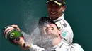 Pebalap Tim Mercedes AMG Petronas F1, Lewis Hamilton, menyemprotkan sampanye ke arah rekan setimnya, Nico Rosberg, setelah memenangi F1 GP Inggris di Sirkuit Silverstone, Inggris. (5/7/2015). (AFP PHOTO/ANDREJ ISAKOVIC)