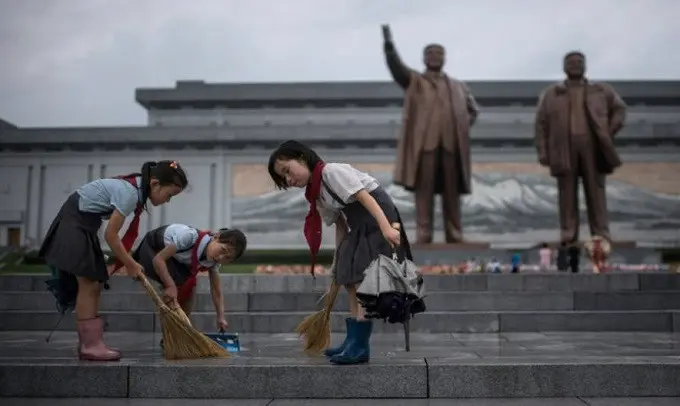 Para siswa membersihkan jalanan di depan patung pemimpin Korea Utara Kim Il Sung dan Kim Jong-Il di bukit Mansu saat negara tersebut menandai 'Victory Day' di Pyongyang (AFP/Ed JONES)